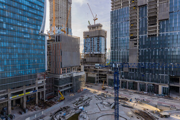 Aerial view of a large construction of a residential area with many multi-storey buildings under construction, a lot of tower cranes, workers, construction equipment at sunset
