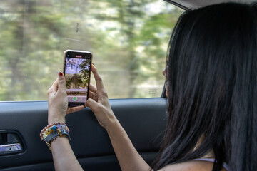 A girl takes a video of a mountain landscape through the window of a moving car, Thailand