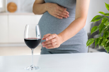 Pregnant woman stretch hand to glass of wine and want to have a drink. Pregnancy and bad habits. Prenatal care and alcohol abuse. - obrazy, fototapety, plakaty