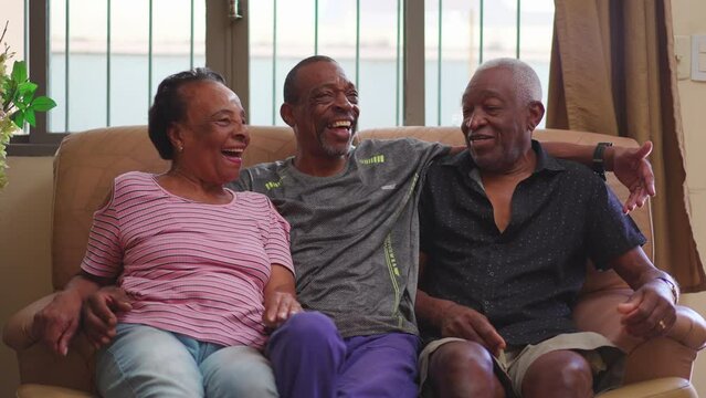 Joyful Brazilian people laughing and smiling seated on couch. A middle-aged son candid interaction with elderly parents at home
