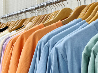 ハンガーにかけて陳列された水色やオレンジ色のTシャツ