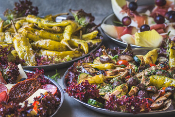 Italian appetizer buffet with grilled vegetables, grilled pepperoni and melon wrapped with ham on gray background, vertical with copy space