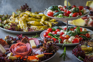 Italian appetizer buffet with grilled vegetables, grilled pepperoni, ham, salami, salad caprese on gray background