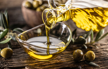 Pouring olive oil from carafe to the glass bowl and in background are olive branches put on table
