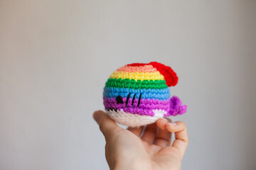 Hand holding rainbow crochet handmade plush shark on white background. Pride symbol