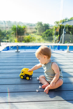 baby sitting on back deck beside glass pool fence playing with truck toy