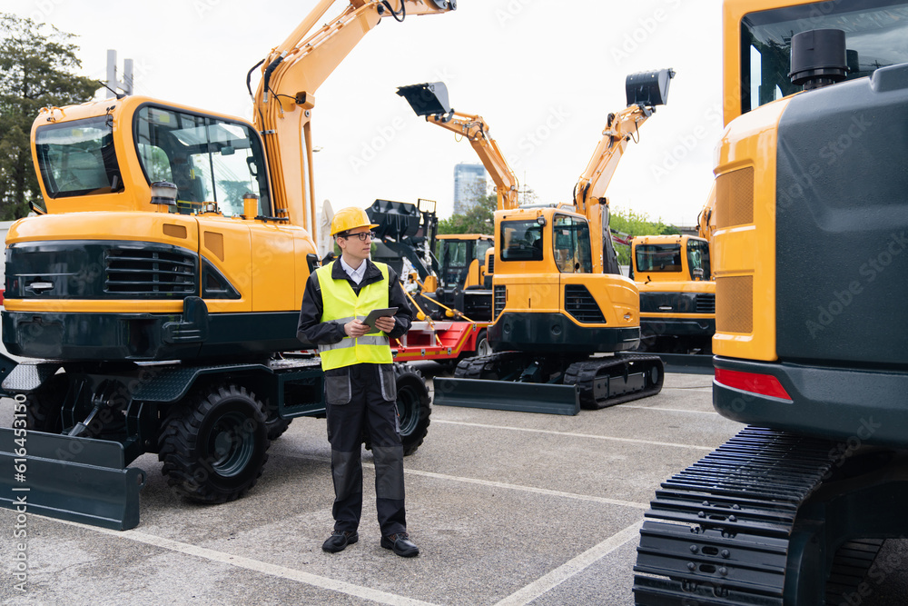 Aufkleber engineer in a helmet with a digital tablet stands next to construction excavators.