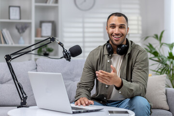Portrait of a young African-American man sitting at home on the sofa in front of a microphone and a...