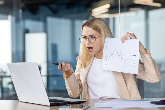 Dissatisfied young businesswoman executive director talks via video call with command, partners, employees and shows documents with graphs of decline, financial crisis, demands explanations