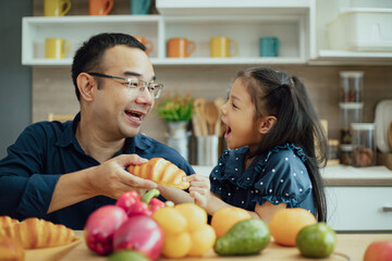 Little cute kid girl daughter and his young father with croissant for breakfast spending time together in the kitchen.
