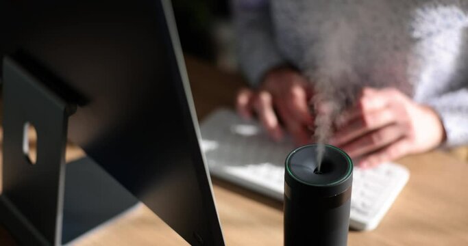 Black humidifier sprays steam on table. Modern air purifier in office workplace