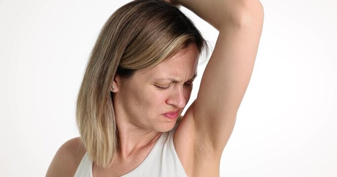 Worried woman with unhappy face checks smell of armpit. Bad underarm odor and bad smelling deodorant