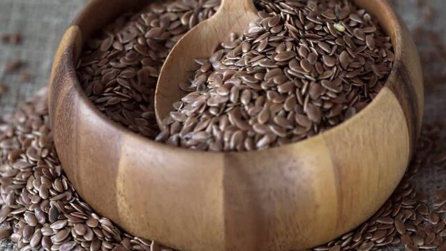 raw flax seeds in a wooden spoon and a wooden bowl