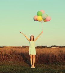 Happy cute smiling young woman with bunch of colorful balloons wearing dress outdoors