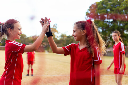 Tween female soccer players high-five in front of the goal net