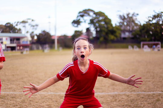 Excited tween girl in a red football uniform yelling with her arms outstretched