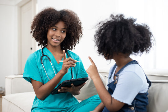 A health visitor with laptop explaining a young girl how to take pills and writing interview with tablet. Home visit health care concept