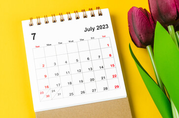 The July 2023 Monthly desk calendar for 2023 year and red tulip on yellow background.