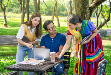 university students learning and doing research together on weekend in the park,group of friends discussing work,there are computer laptops, text books,coffee cups on table