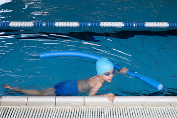 Close up boy swimmer o school boy learning how to swim in a pool wearing in swimming cap and goggles
