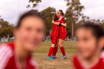 Two tween girls in a football team hug to celebrate a win