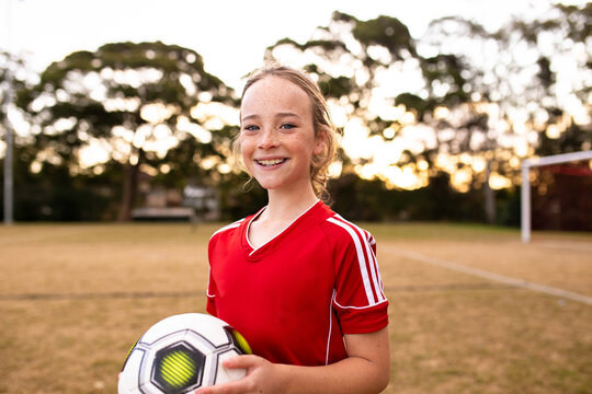Portrait of tween girl in a red uniform holding a football and smiling