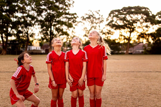 A tween girls football team looking up waiting for a ball to drop back into the frame