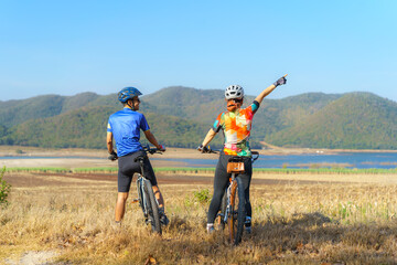 Asian cyclist couple looking at lake and mountain view and chatting while taking a break from the morning bike ride..