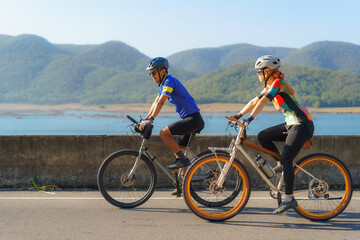 Asian cyclist couple riding together for exercise around the lake in the morning with beautiful mountain view in the background...