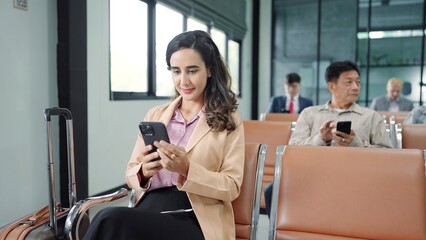 Young hispanic latin woman passenger using smartphone while sitting on chair in terminal departure gate waiting flight at international airport