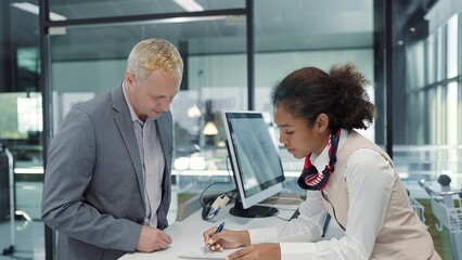 American african women airline ground staff worker giving boarding pass or ticket to caucasian businessman passenger in airport check in counter. Business trip concept