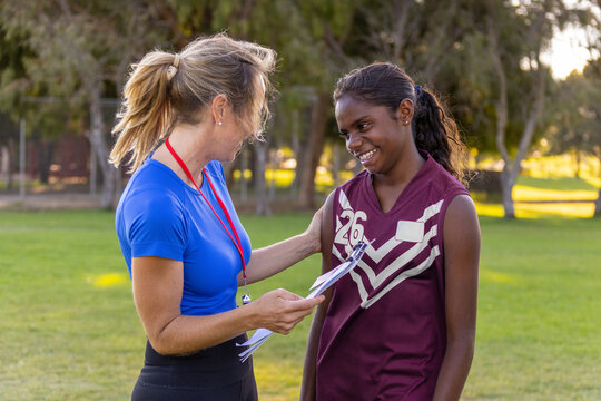 female footy coach speaking with encouragement to shy aboriginal girl