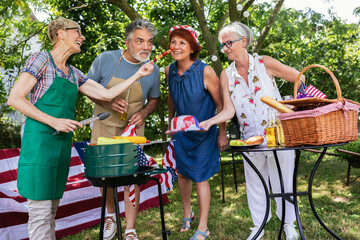 Naklejka na ściany i meble A group of elderly people celebrates the 4th of July in a backyard while making barbeque.