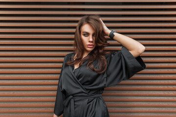 Styling beauty young stylish chic lady with brunette hairstyle in a fashion elegant black suit stands near a rusty metal wall in the city