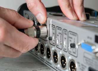 A male hand unplugs a male XLR cable - obrazy, fototapety, plakaty