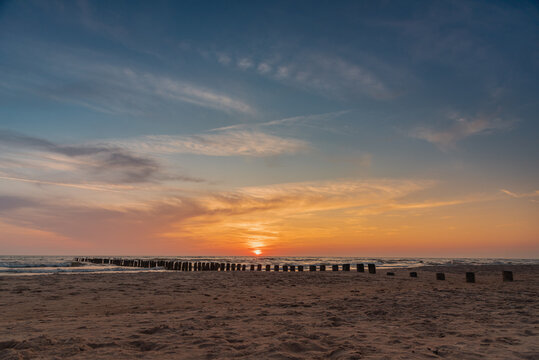 Sunset on Baltic sea shore with old wooden breakwater poles sticking out of the sea in Bernati, Latvia