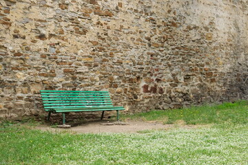 Green bench in front of an old wall, relaxing quiet garden.