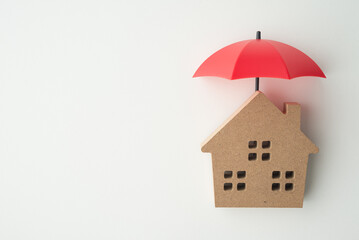 Red umbrella cover home model on blue background copy space. House, real estate, property insurance...