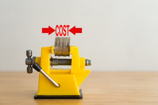 Bench vise clamp press coins for control cost reduction with white wall background on wooden table. Concept of cost reduction, cost cut in business or production, optimize continuous improvement.