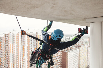 Man industrial mountaineer worker in uniform and helmet hanging over, working on residential...