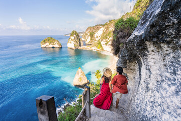 Young couple traveler relaxing and enjoying the beautiful view at diamond beach in Nusa Penida island, Bali - obrazy, fototapety, plakaty
