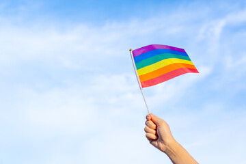 rainbow gay flag in hand waving against clear blue sky space, LGBTQ people doing activities celebrating equality sexual freedom, diversity of genders, love and protecting the rights of individual