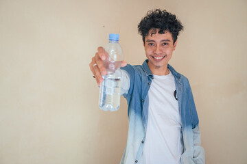 Young curly man with denim clothes hold a bottle water. Smile, cheers and happy expression. The photo is suitable to use for mineral water bottle promotion and healthy life advertising.