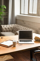 Work table with laptop, note book and white cup. Nice soft light. Image with grain. Blurred focus. Place for text.