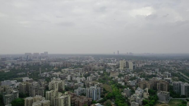 aerial drone shot on a cloudy overcast day showing cityscape of gurgaon with small houses, skyscrapers with homes houses, offies and shopping centers in the city of gurgaon delhi India