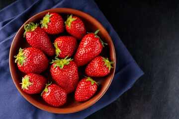 Fresh ripe strawberry in bowl on dark background. Clay bowl with strawberries on blue napkin. Copy space. Top view