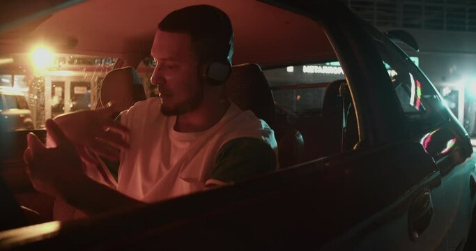Man sitting in car and training dance moves with music on headphones