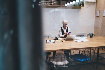 Aged businesswoman using smartphone in modern conference room