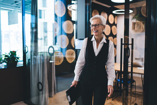 Aged businesswoman laughing while standing near glass wall