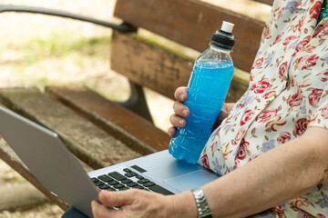 An elderly person with a laptop and and sport drink in hand.